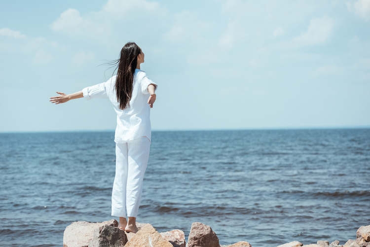 rear view of young woman enjoying sea with arms outstretched on beach